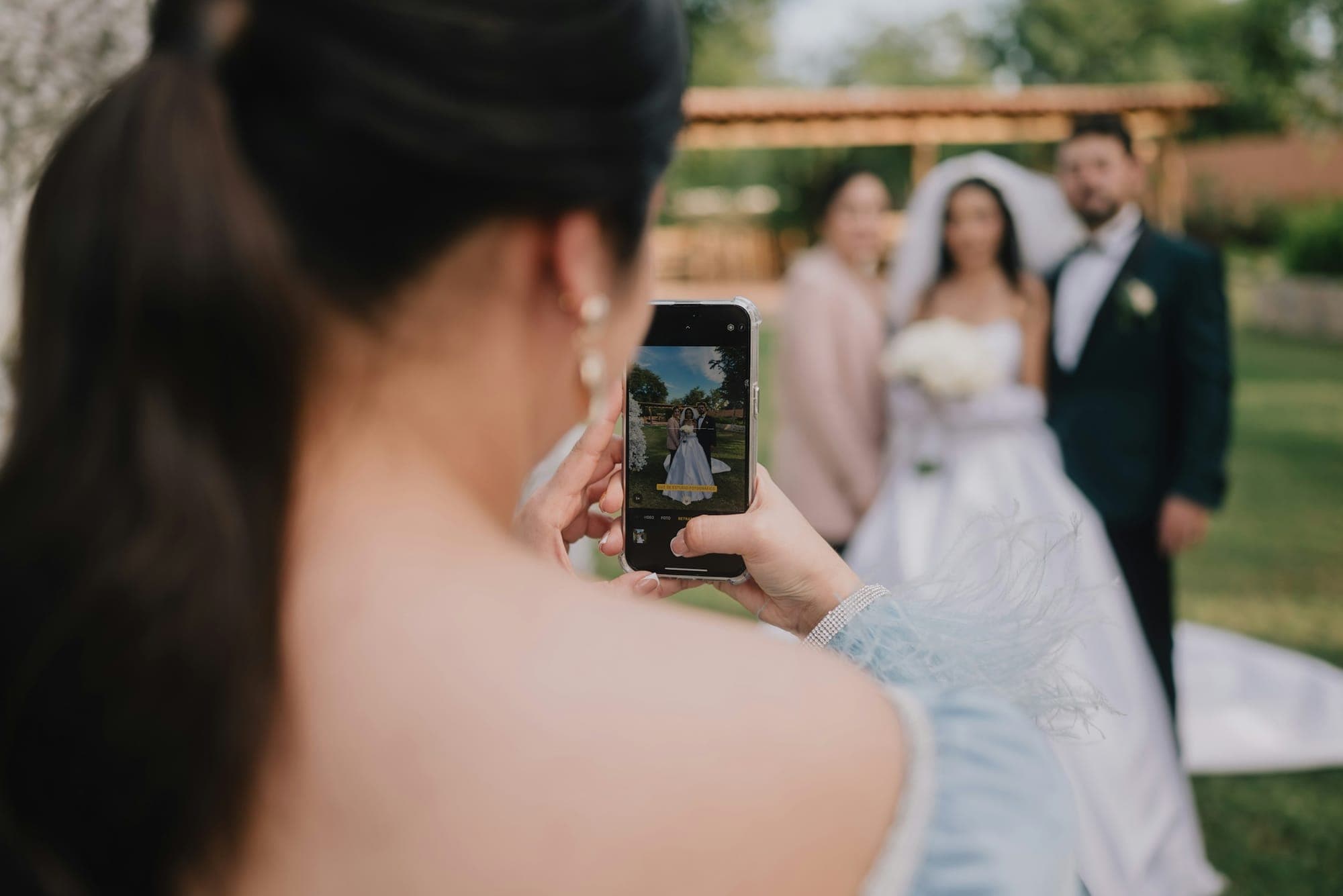 Hochzeitsgast fotografiert das Brautpaar im Garten mit dem Smartphone